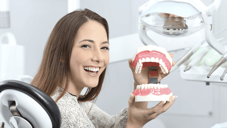 Younger woman smiling and holding teeth display, tuscaloosa al