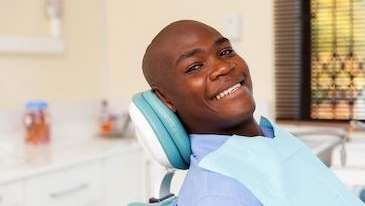 Black man sitting in chair smiling after using clear aligners, tuscaloosa al